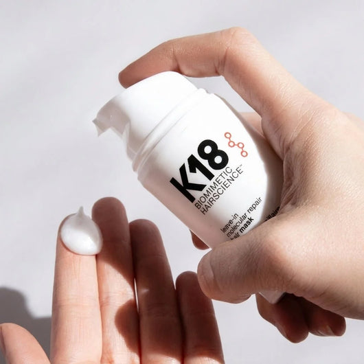 Eine Hand drückt eine Portion der K18 Leave-in Haarmaske aus der weißen Produktflasche auf die andere Handfläche.