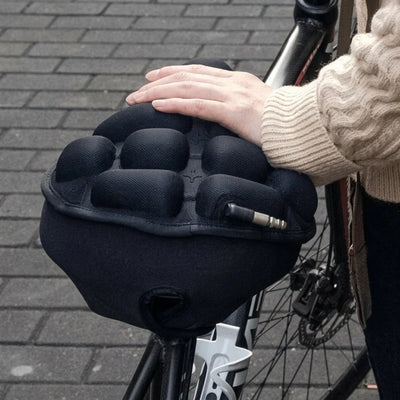 Druckentlastendes Fahrradsattelkissen mit Stoßdämpfung, das von einer Hand auf einem Fahrradsattel gehalten wird.