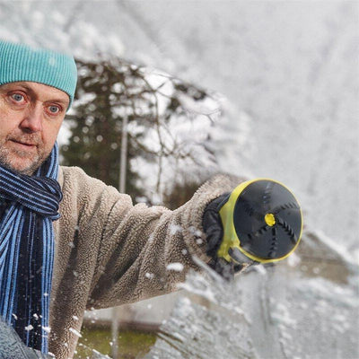 Ein Mann mit Mütze und Schal benutzt einen elektrischen Eiskratzer, um eine vereiste Autoscheibe zu reinigen.