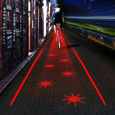 Ein Fahrradfahrer bei Nacht auf einem dunklen Weg mit einem LED-Rücklicht, das rote Laserlinien und Sterne auf den Boden projiziert.