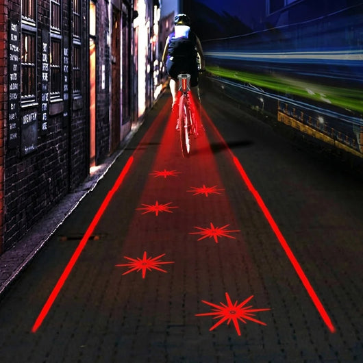 Ein Fahrradfahrer bei Nacht auf einem dunklen Weg mit einem LED-Rücklicht, das rote Laserlinien und Sterne auf den Boden projiziert.
