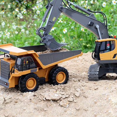 Ein ferngesteuerter Bagger lädt Sand auf einen Muldenkipper in einer Gartenumgebung.