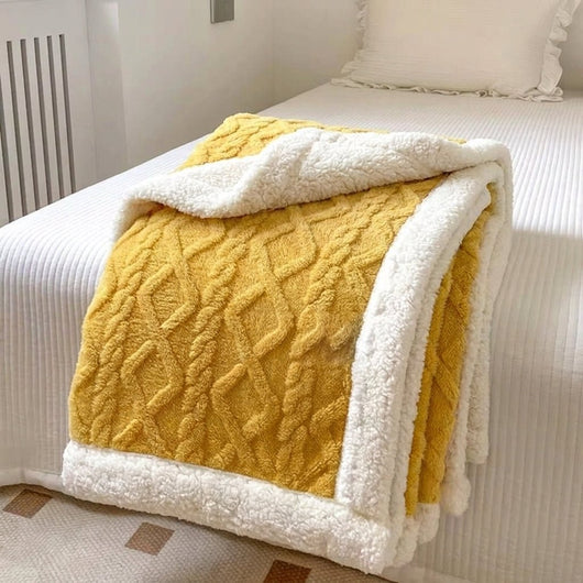 Gelbe Fleecedecke mit Lammwolle und Zopfmuster, die gefaltet auf einem weißen Bett liegt.