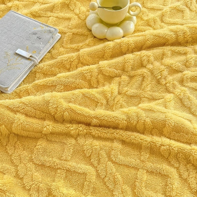 Eine gelbe, flauschige Fleecedecke mit Lammwolle-Optik, daneben ein graues Notizbuch und eine Tasse Tee auf einem Untersetzer.