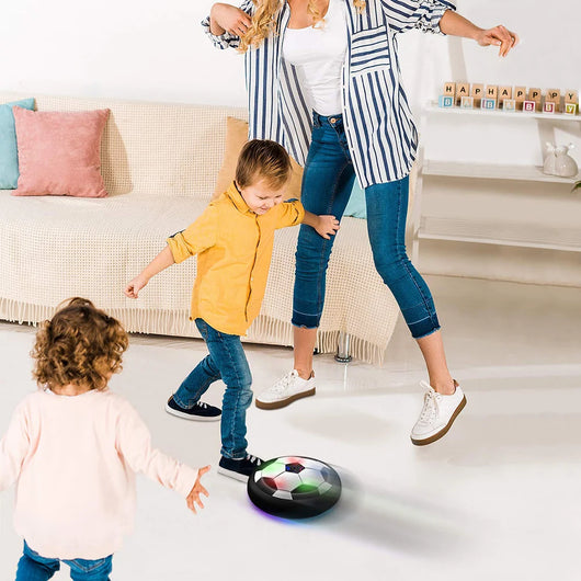 Eine Mutter spielt mit ihren zwei Kindern in einem Wohnzimmer mit einem leuchtenden Hoverball Fußball.