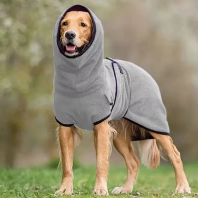 Ein Hund trägt einen grauen, wasserdichten Wintermantel mit Kapuze auf einer Wiese.