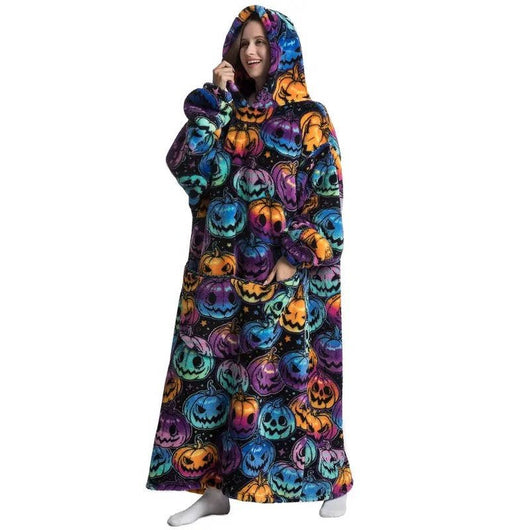 Eine Frau trägt eine übergroße Kapuzendecke mit buntem Kürbis-Muster, Fleece-Futter und einer Kängurutasche.