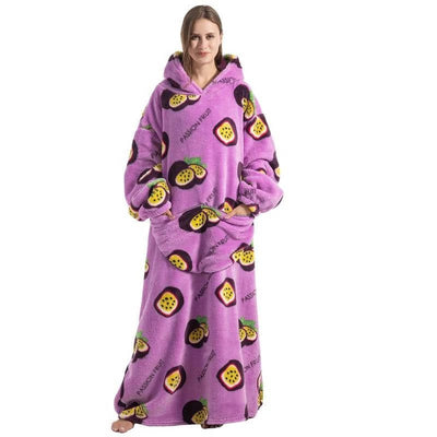 Eine Frau trägt eine lange, lilafarbene Kapuzendecke mit Passionsfrucht-Muster, Kängurutasche und elastischen Bündchen.