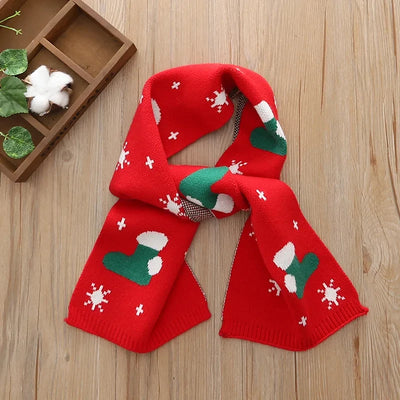 Roter Kinderschal mit weihnachtlichem Muster aus grünen Socken und weißen Schneeflocken auf einem Holzhintergrund.