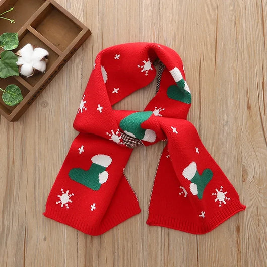 Roter Kinderschal mit weihnachtlichem Muster aus grünen Socken und weißen Schneeflocken auf einem Holzhintergrund.