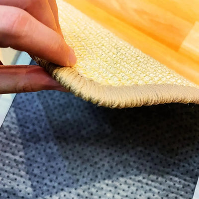 Nahaufnahme einer Hand, die den Rand eines robusten Sisal-Kratzbretts für Katzen anhebt.
