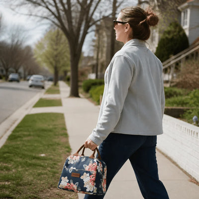Eine Frau geht mit einer kleinen, blumigen Kühltasche in der Hand einen Gehweg entlang.