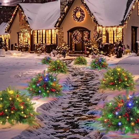 Beleuchtete künstliche Tannenbäume als Wegbeleuchtung vor einem weihnachtlich geschmückten Haus im Schnee