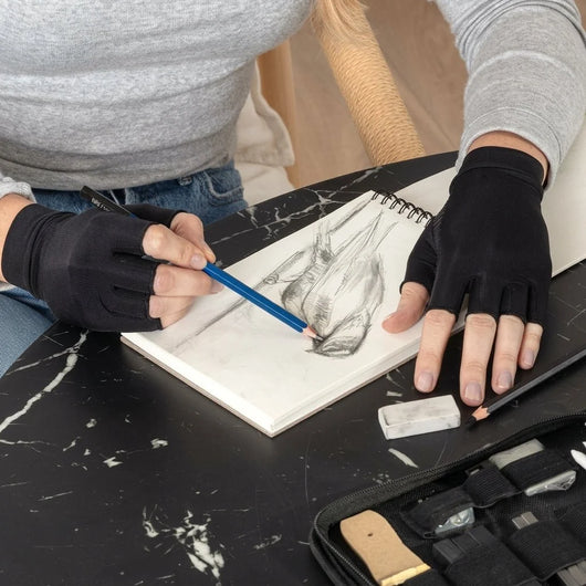 Kupferkompressionshandschuhe mit offenen Fingern bei einer Person, die in einem Skizzenbuch zeichnet.
