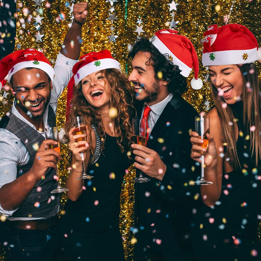 Vier Freunde feiern mit Sekt und leuchtenden LED-Weihnachtsmützen auf einer Party.