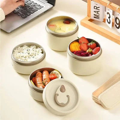 Isoliertes Lunchbox-Set aus Edelstahl mit drei stapelbaren Behältern für warme und kalte Speisen auf einem Schreibtisch.