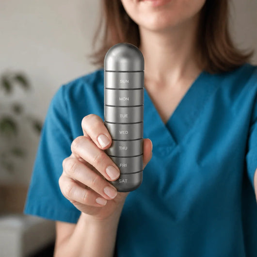 Eine Person in blauer Arbeitskleidung hält einen stapelbaren Pillenorganizer aus Aluminium mit Wochentagsbeschriftung.