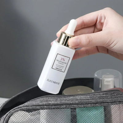 Eine Hand hält eine kleine, weiße Flasche mit Nicotinamid-Essenz über einer offenen, grauen Kosmetiktasche.