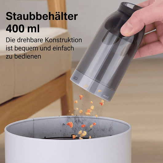 Ein Handstaubsauger wird über einem Mülleimer entleert, um den 400 ml Staubbehälter einfach zu reinigen.