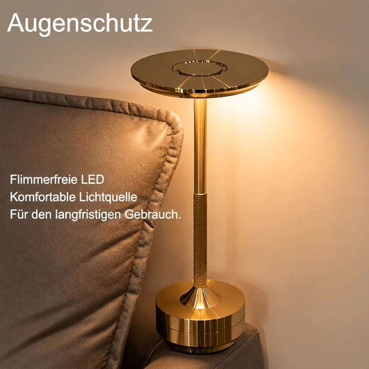Eine elegante goldene kabellose Tischleuchte steht neben einem Polstermöbel und spendet warmes Licht.
