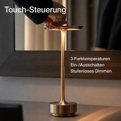 Eine Hand bedient die Touch-Steuerung einer eleganten, kabellosen Tischleuchte mit goldfarbenem Metallgehäuse.